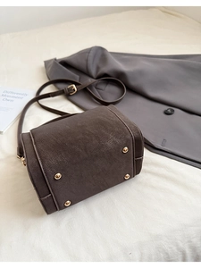 Detail view of dark brown textured leather crossbody bag with gold protective base feet