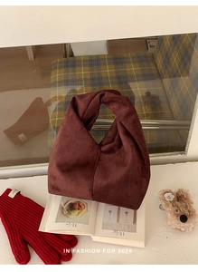 Close-up of dark burgundy suede handbag featuring a unique knotted handle design