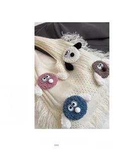 Detail of white knit handbag featuring colorful plush cartoon eyes and long fringe trim