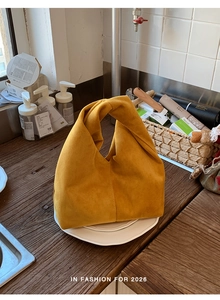 Detail of a yellow suede cloud bag featuring a unique knotted handle design and soft texture
