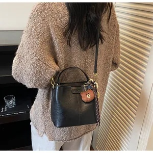 Detail of black bucket bag with plush bear charm and check scarf in home setting