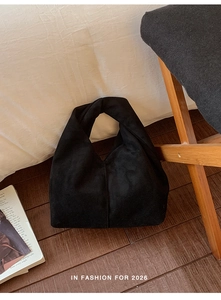 Detail of minimalist black suede tote bag featuring a unique twisted knot handle design