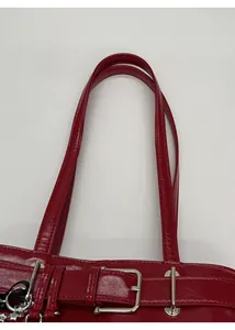 Detail of red glossy patent leather handbag with silver metal buckle and dual handles