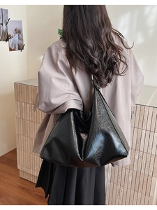 Detail of a large black vintage hobo bag in wrinkled patent leather worn by a model