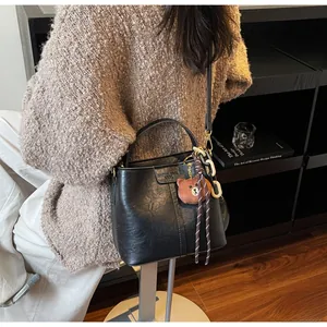 Detail of black leather bucket bag featuring metal chain and cute brown bear charm