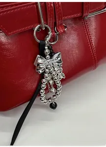 Macro detail of silver bow pendant with beaded tassels on red leather shoulder bag