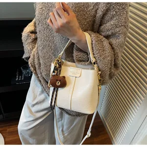 Detail of a creamy white leather bucket bag with a plush bear charm in a cozy room