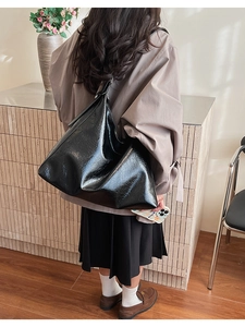 Rear view of a minimalist large black hobo bag in glossy wrinkled leather on a model