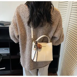 Close-up of white PU leather bucket bag with vertical stitching and brown bear charm