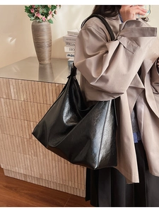 Detail of a large black tote bag in glossy wrinkled leather with zipper and thin straps