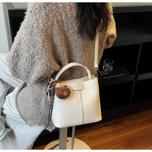 Detail view of cream bucket bag in pebble leather with bear charm on a model