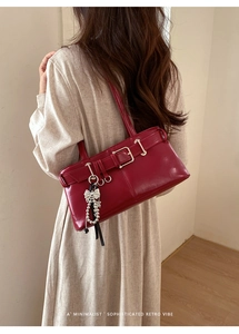Deep red leather underarm bag with silver bow charm and pearl detail on a model