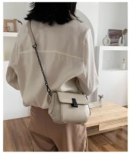 Detail of minimalist cream crossbody bag with black chain strap shown on a shoulder