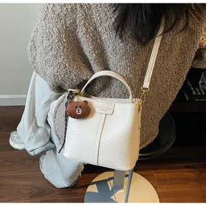Detail view of white bucket bag with litchi texture and brown bear plush charm