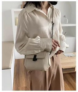 Close-up of cream crossbody bag featuring a black metal trapezoid buckle and chain strap