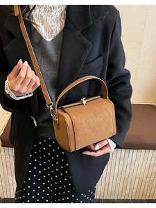 Close-up of brown vintage square handbag with metal clasp worn by a fashion model