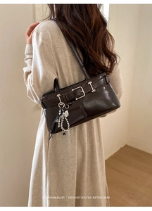 Detail of dark brown patent leather underarm bag with silver charms on a beige dress