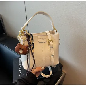 Close-up of beige bucket bag with Fashion trend text, bear charm, and woven rope detail
