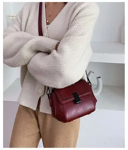 Detail view of burgundy crossbody square bag with elegant black clasp on beige cardigan