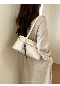 Detail of minimalist cream shoulder bag with belt buckle and elegant ribbon charm