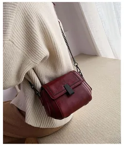 Detail of burgundy leather crossbody bag with black metal chain strap and matte buckle