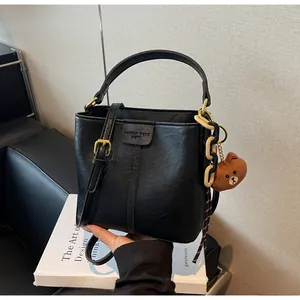 Detailed close-up of matte black bucket bag with gold hardware and plush bear charm