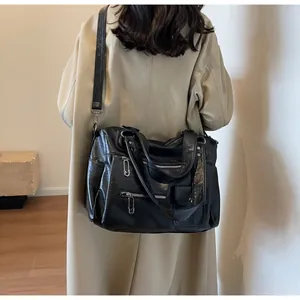 Detail of black multi-pocket PU leather shoulder bag with rivet accents on a beige coat