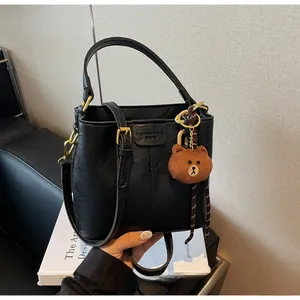 Detail of black bucket bag with embossed text and a cute brown plush bear pendant