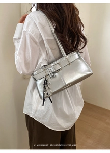 Detail of silver underarm bag with belt buckle and ribbon charm on white shirt