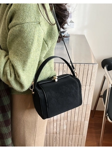 Close-up of a vintage black leather frame bag styled with a green knit sweater and brown skirt