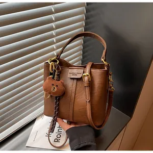 Close-up of brown leather bucket bag with teddy bear charm and embossed logo detail
