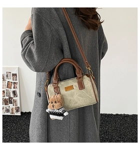 Detailansicht der graugrünen Boston-Tasche mit braunen Ledergriffen und Bärenanhänger