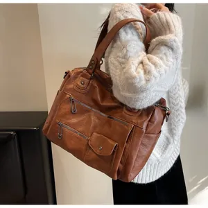 Close-up of caramel leather tote bag featuring retro zippers and pin buckle details