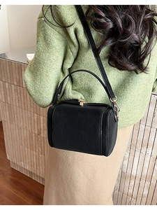 Woman carrying a black leather box handbag with gold buckle in a street style setting