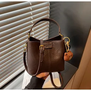 Detail of dark brown leather bucket bag featuring a plush bear charm and crossbody strap