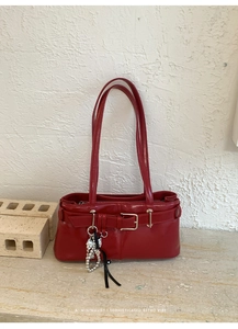 Macro shot of red glossy leather shoulder bag with silver heart charm and metal buckle detail