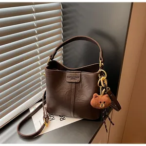Detail of vintage brown bucket bag with natural leather texture and plush bear charm