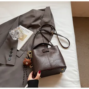 Detail of vintage brown leather bucket bag with plush bear charm and metallic feet