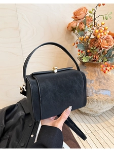Detail of black box-shaped handbag with textured faux leather and gold metal clasp