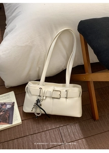 Detail of a minimalist white leather shoulder bag with silver chain and bow charm detail