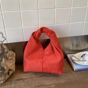 Close-up of red suede cloud bag showing soft pleated texture and decorative knot handle