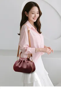 Detail of burgundy ruched cloud bag with light brown handles on an elegant model