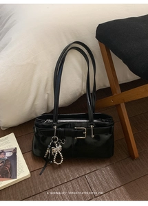 Detail of black glossy shoulder bag with silver butterfly charm on dark wood floor