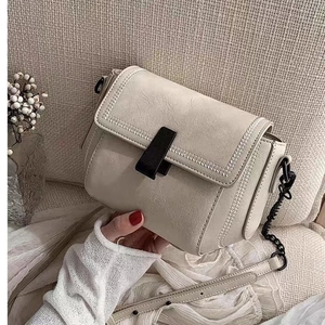 Beige textured PU leather crossbody bag with black chain strap on a soft beige sofa