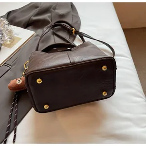 Detail view of deep brown bucket bag with gold-tone base studs and teddy bear charm