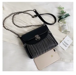 Detailed view of black striped crossbody bag size compared with a smartphone