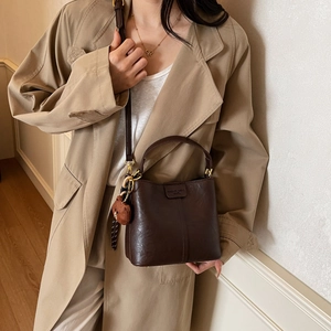 Vintage dark brown bucket bag with plush bear pendant shown on beige coat outfit