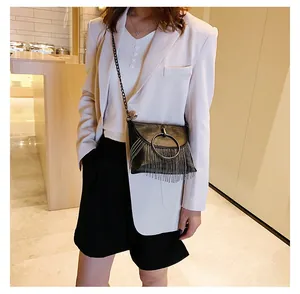 Close-up of black PU leather crossbody bag with metal ring and tassel on white blazer