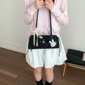 Détail du sac bandoulière en daim noir avec broderie florale et breloque en dentelle blanche