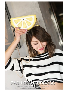 Detail of yellow lemon-shaped crossbody bag with metal chain strap worn by a model